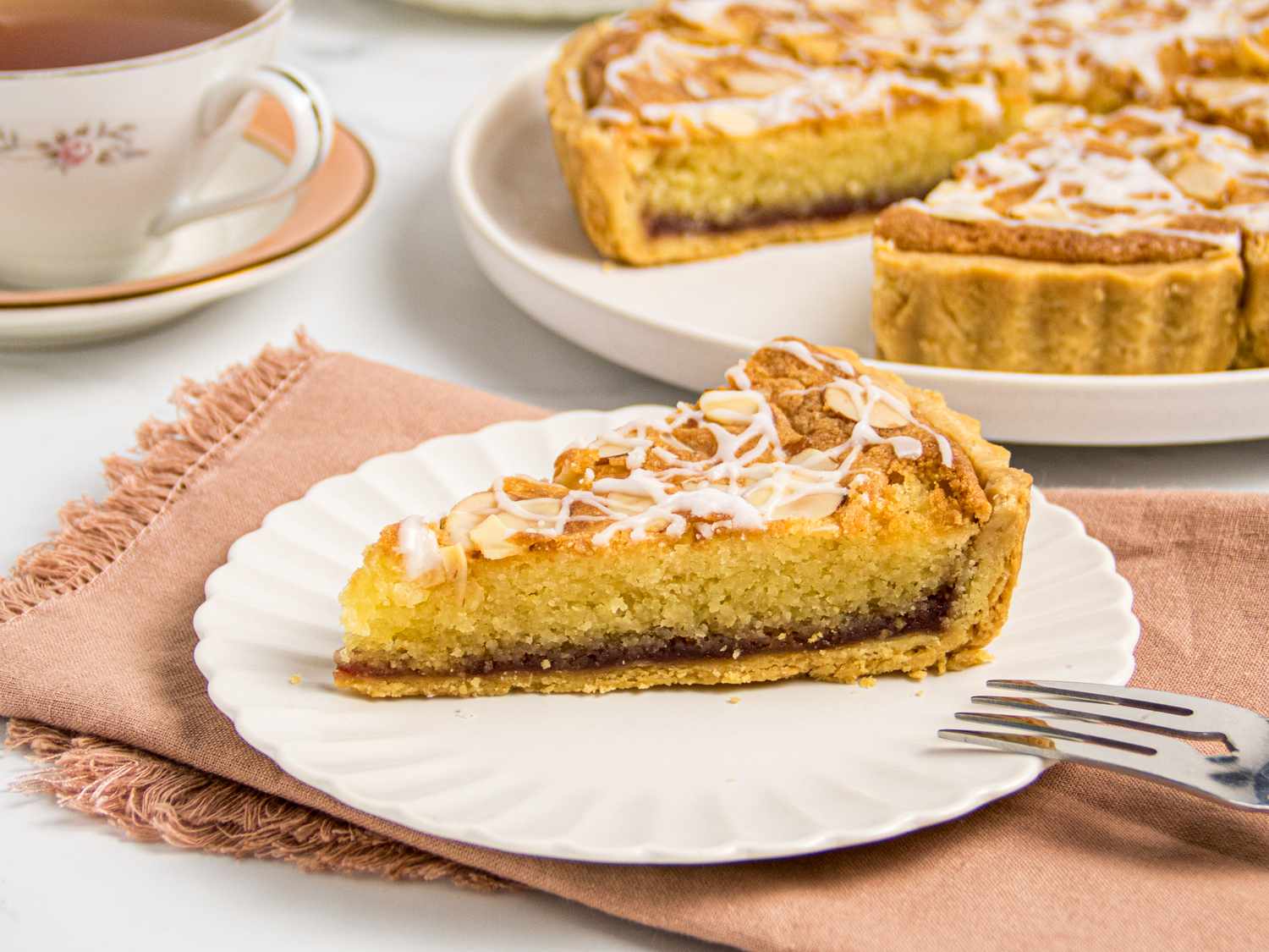 Slice of tart on a plate, tart and tea in background