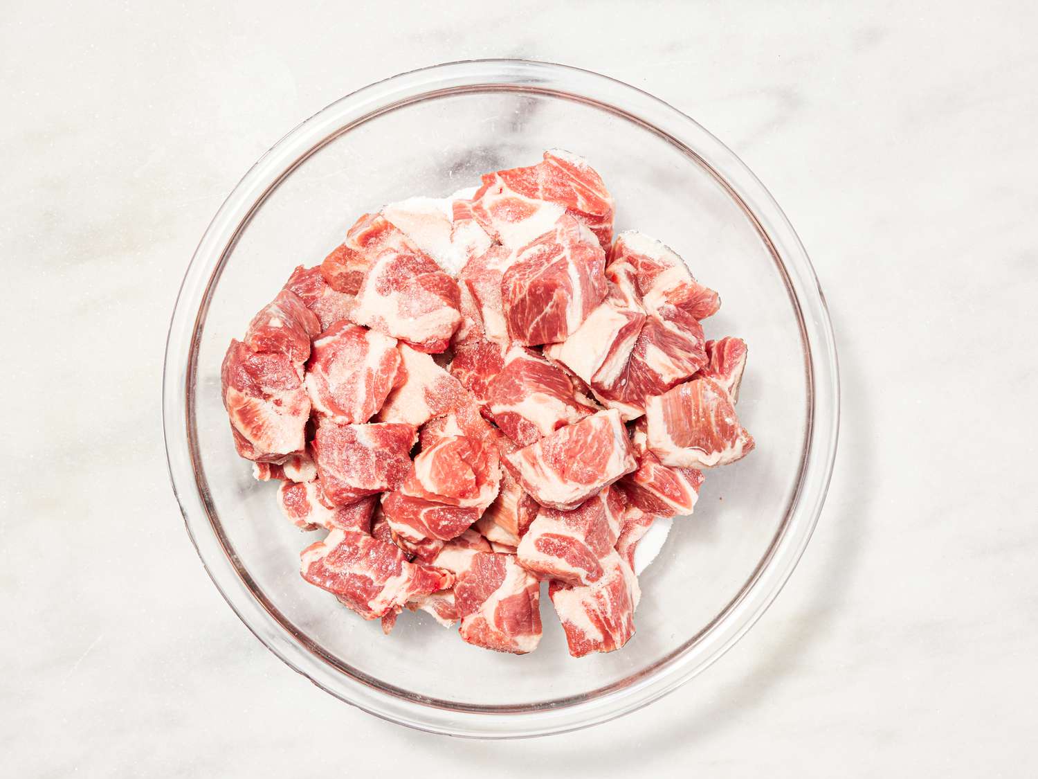 Overhead view of combining pork shoulder with salt in a bowl.