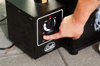 A person turns the Bradley Smoker 4-Rack Outdoor Electric Smoker, Natural Draft Smoker (BS611) on