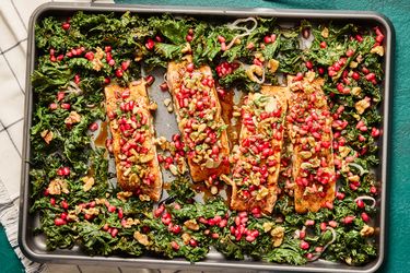 Salmon fillets topped with pomegranate seeds and greens on a baking sheet