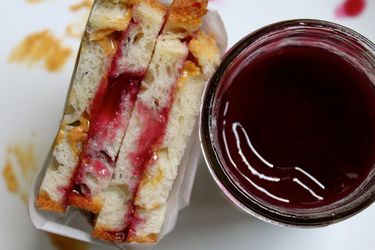 A peanut butter and jelly sandwich next to a jar of grape jam. 