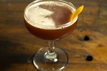 A pomegranate bourbon cocktail, served in a coupe glass with a lemon twist.