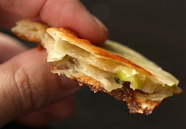 A hand holding a slice of scallion pancake showing five layers.