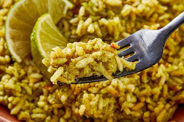 A fork holding a portion of seasoned rice with lime slices in the background