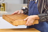 A person holding a Boardsmith Maple End-Grain Cutting Board in a kitchen setting wearing a striped shirt and an apron
