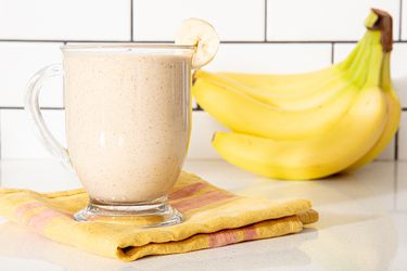 Banana smoothie in a glass cup with bananas in the background.
