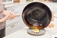 A person slides a cooked egg from the Joyce Chen Carbon Steel Wok onto a plate
