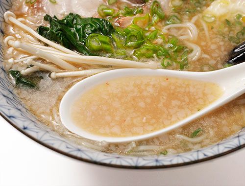 Spooning fat-flecked pork broth from a bowl of ramen.