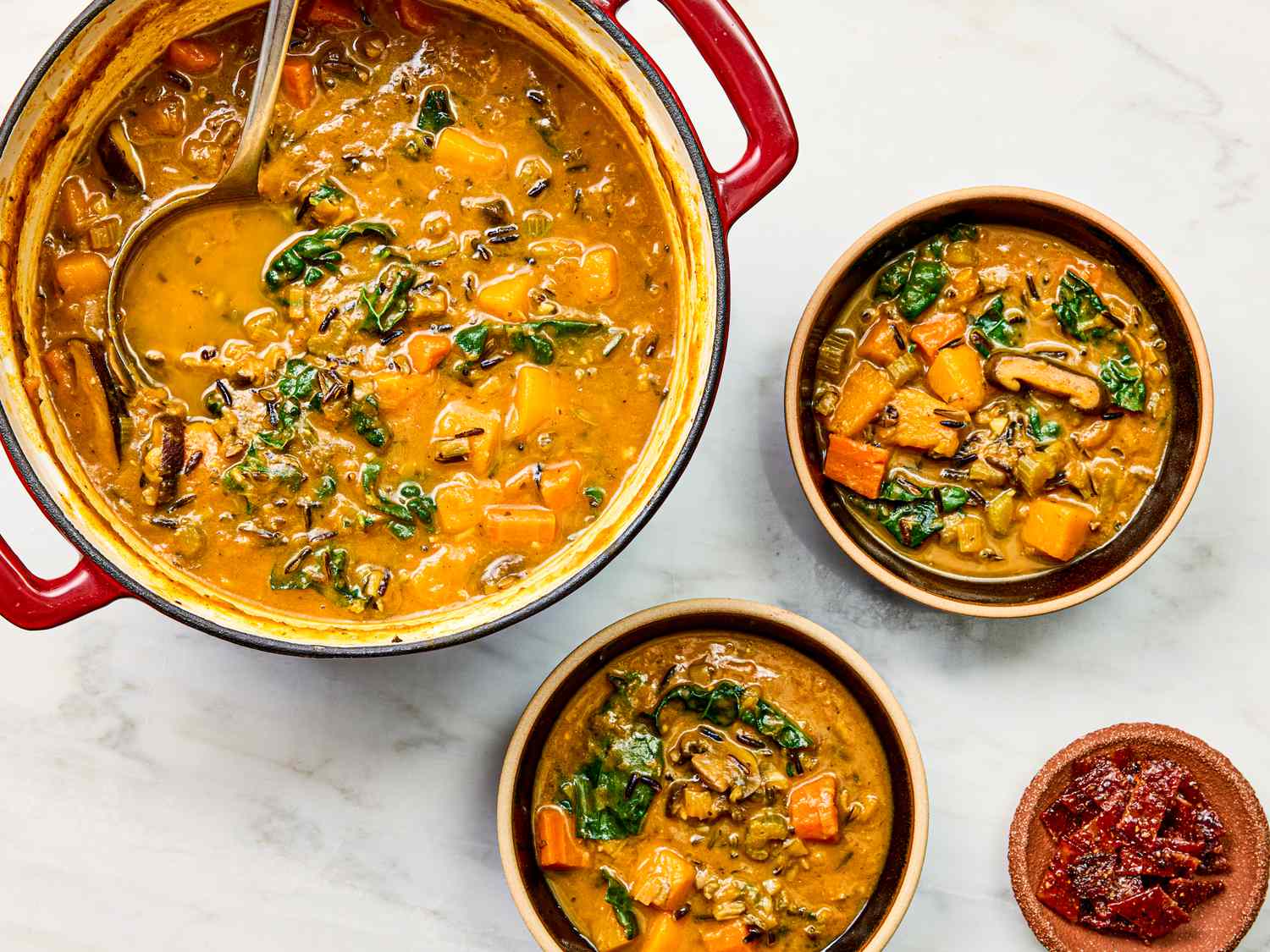 A pot and bowls of soup with various ingredients like vegetables and grains