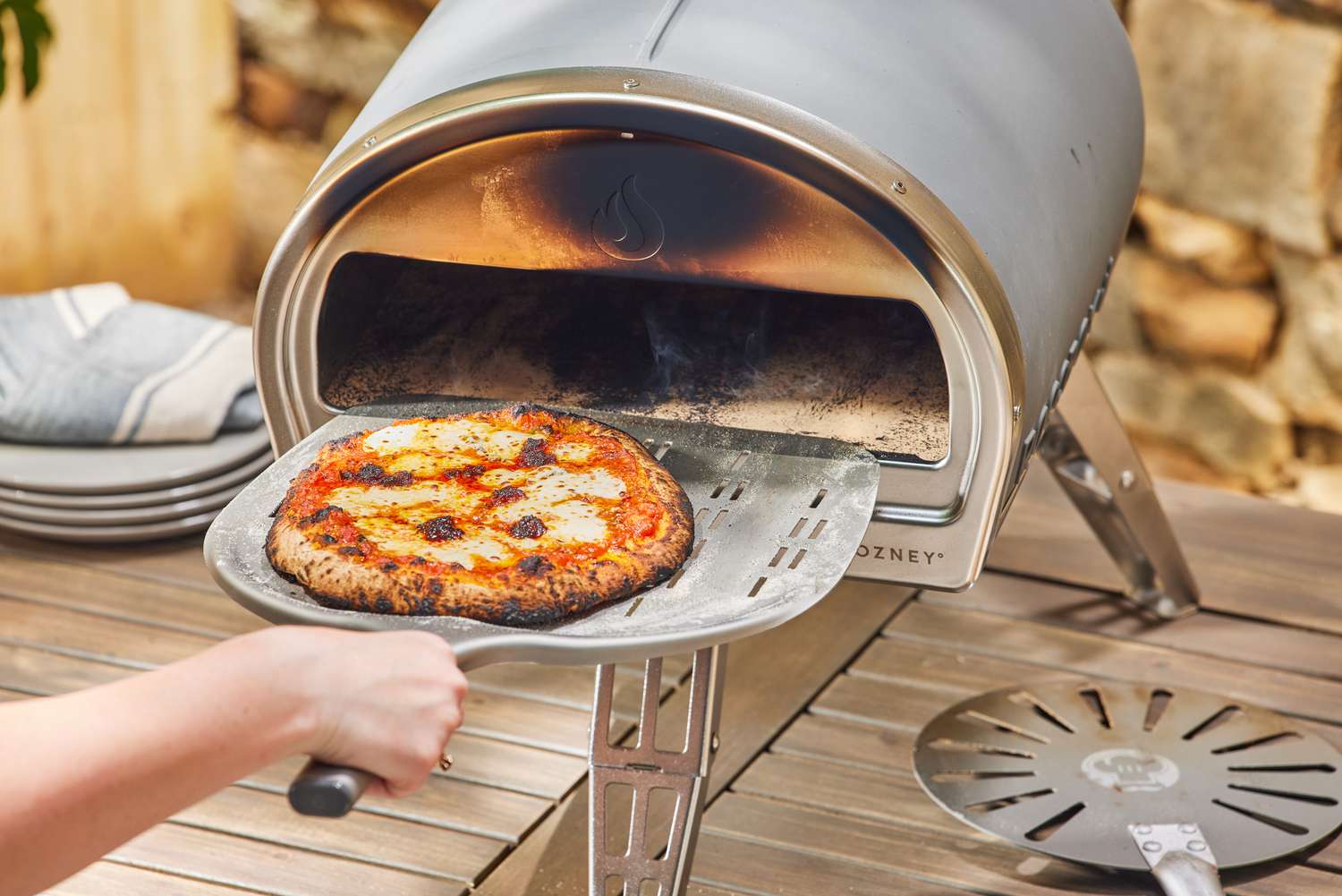 A hand removing a pizza from the Gozney Roccbox Pizza Oven