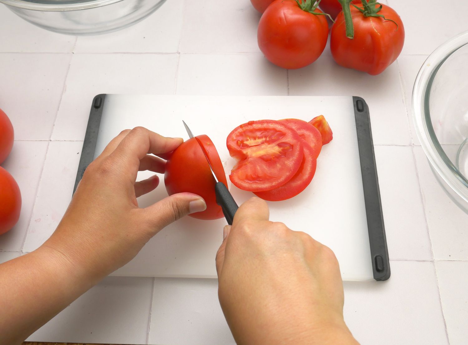 a person slicing a tomato with a paring knife
