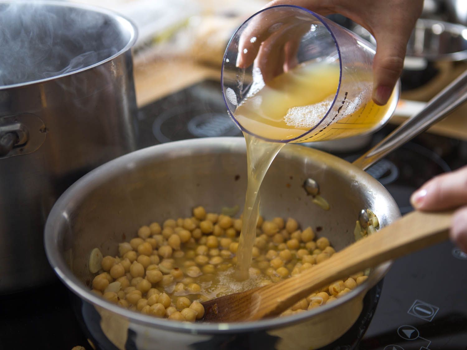 Chickpeas and some of their cooking liquid are added to the saucepan.