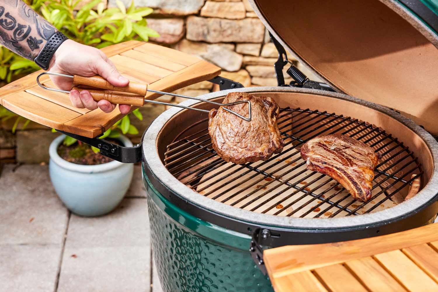 A person removes meat from the Big Green Egg Large Charcoal Kamado Grill and Smoker