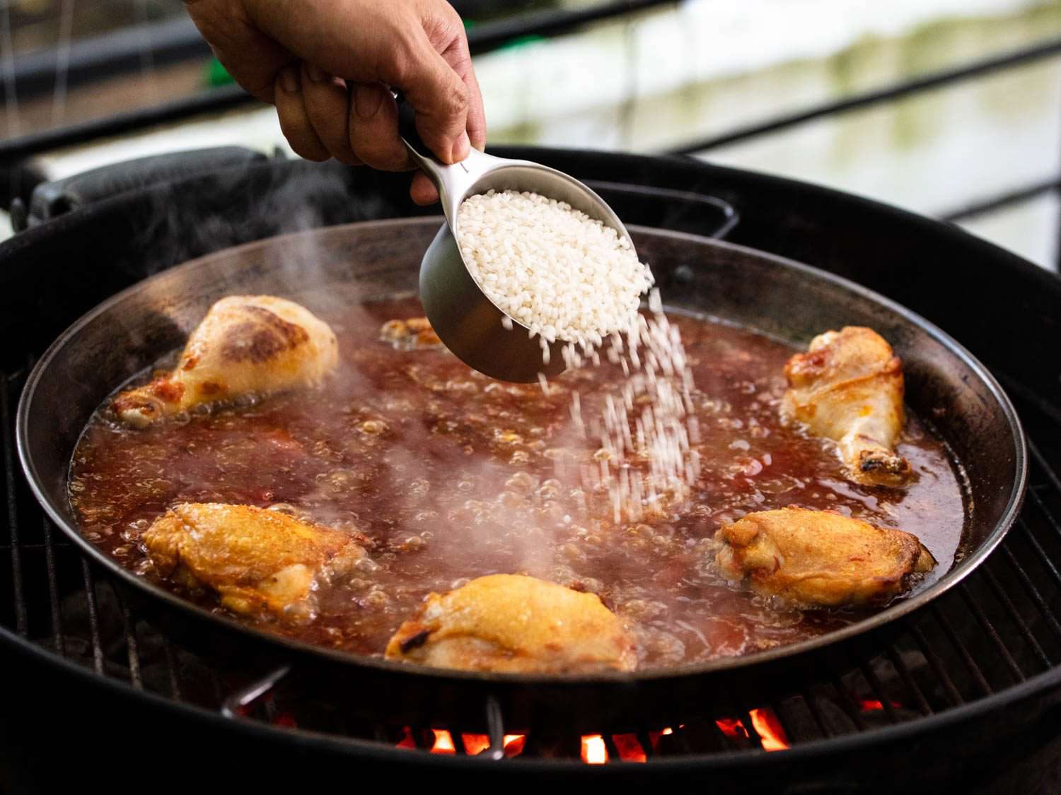 Adding rice to boiling liquid in the paella pan.