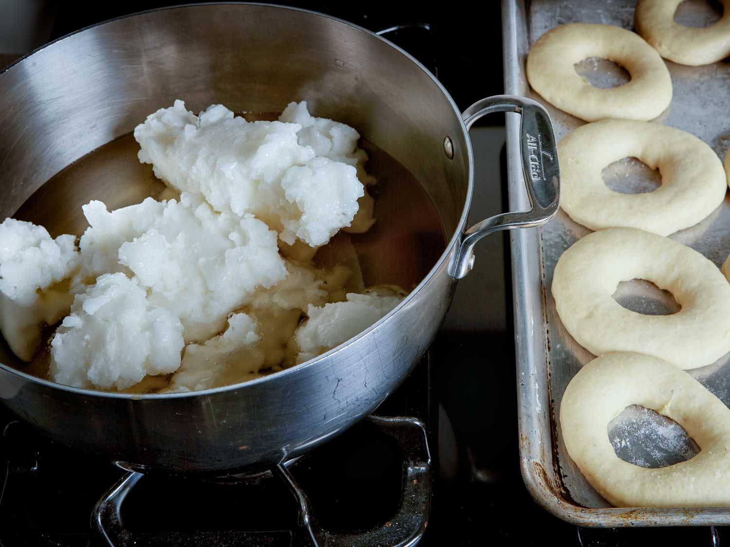 solid coconut oil in a large dutch oven, half melted, with a tray of doughnut dough nearby