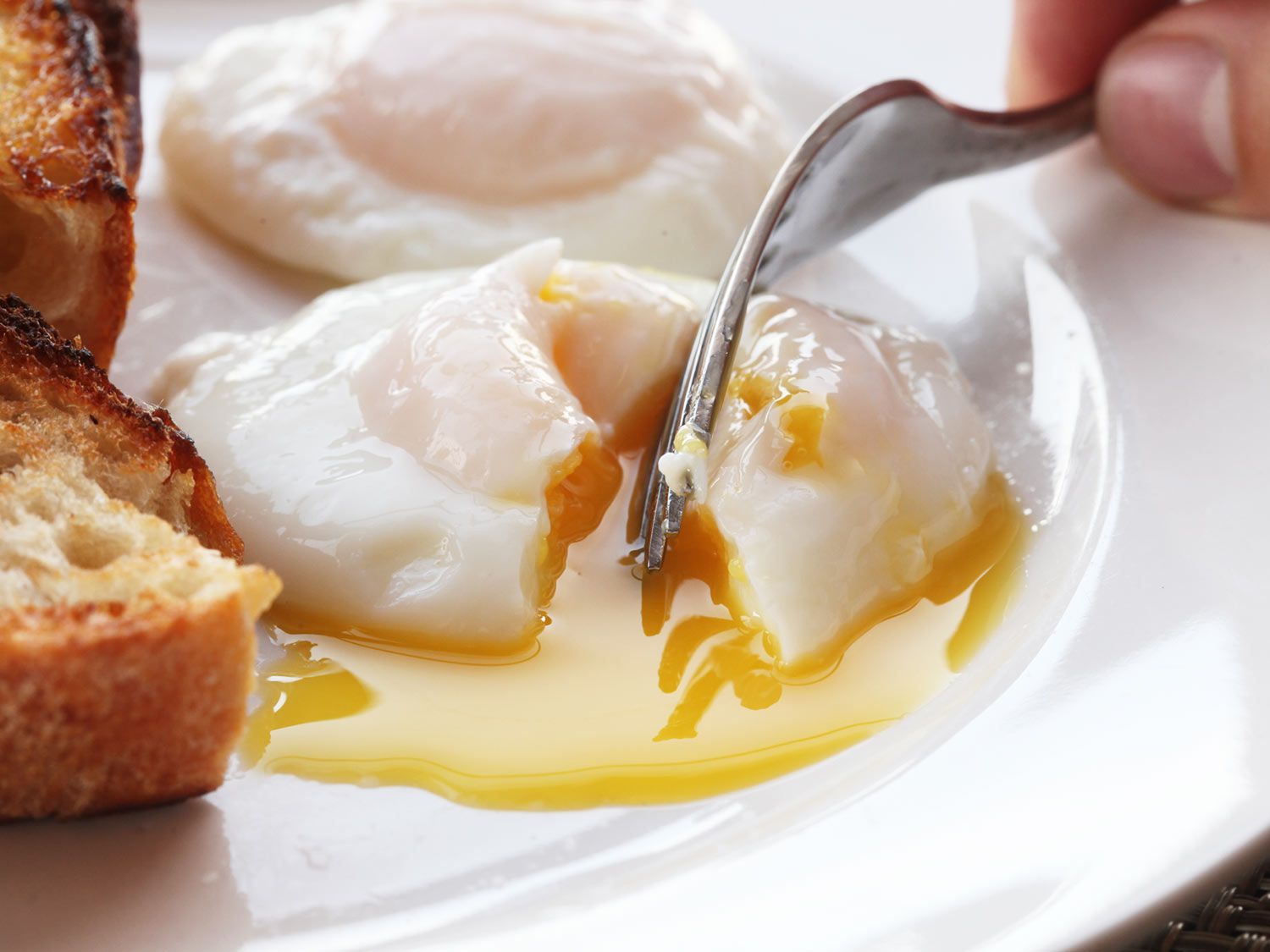 Fork breaking into a runny poached egg.