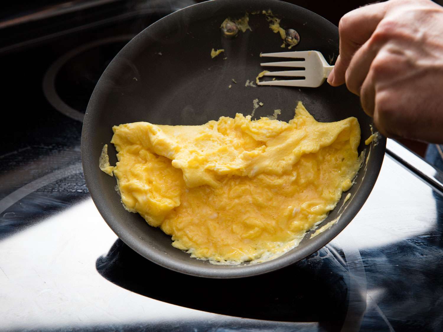 Hand using a fork to flip an omelet in a nonstick skillet