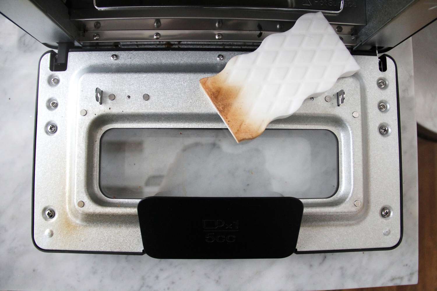 using a magic eraser to clean the window on a toaster oven