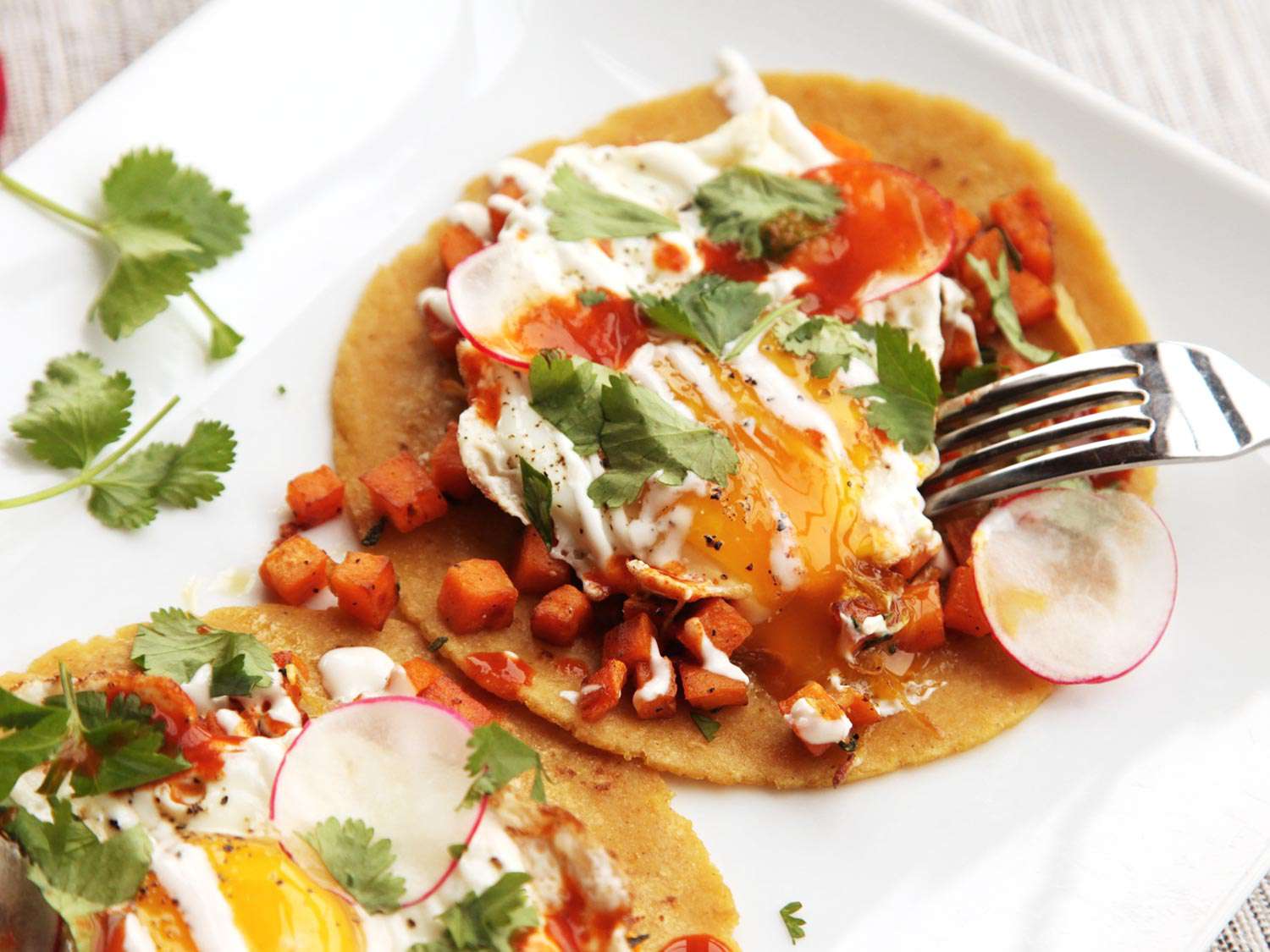 Fork piercing yolk of fried egg on top of sweet potato taco