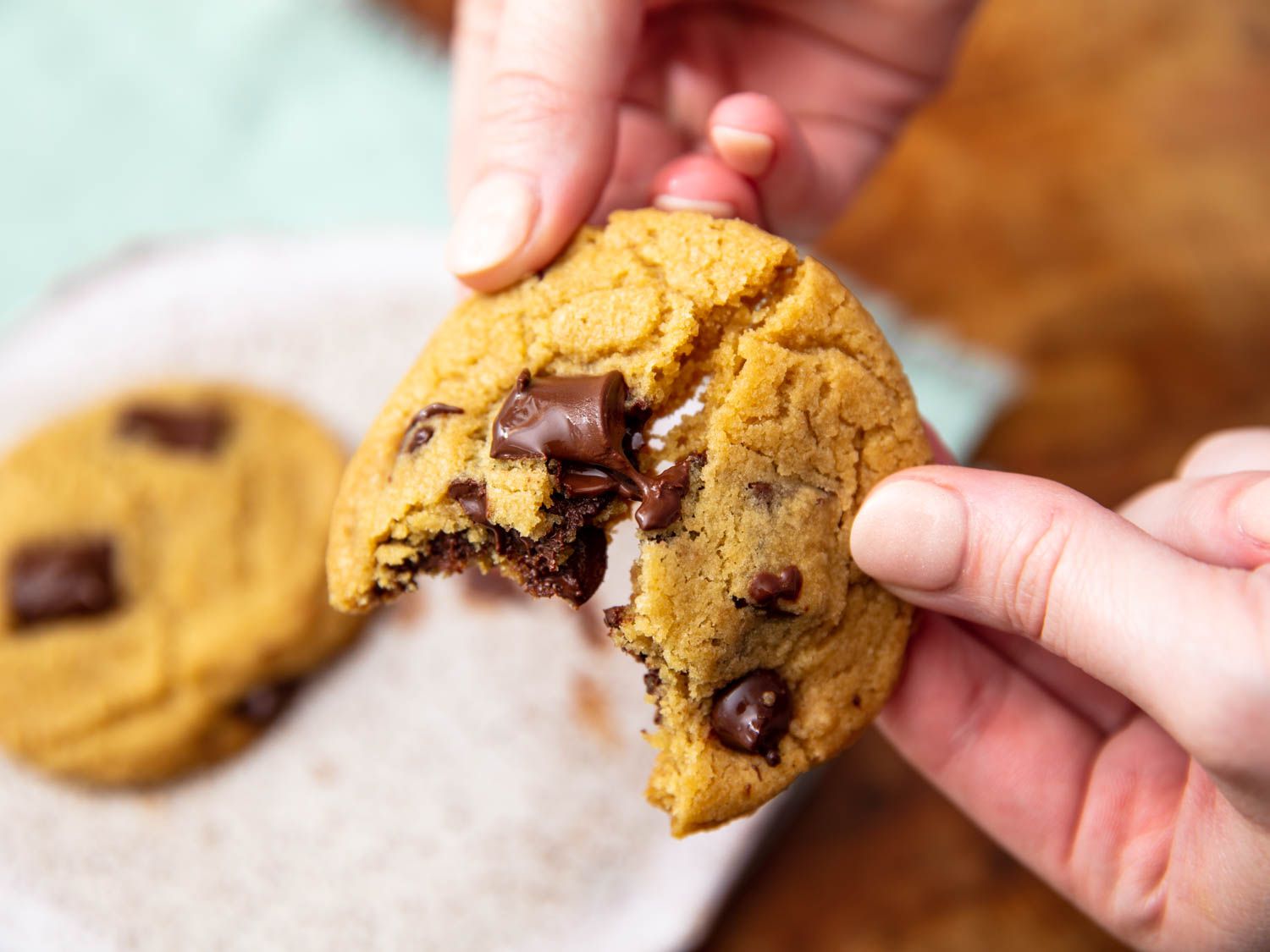 Hands breaking apart an olive oil chocolate chip cookie
