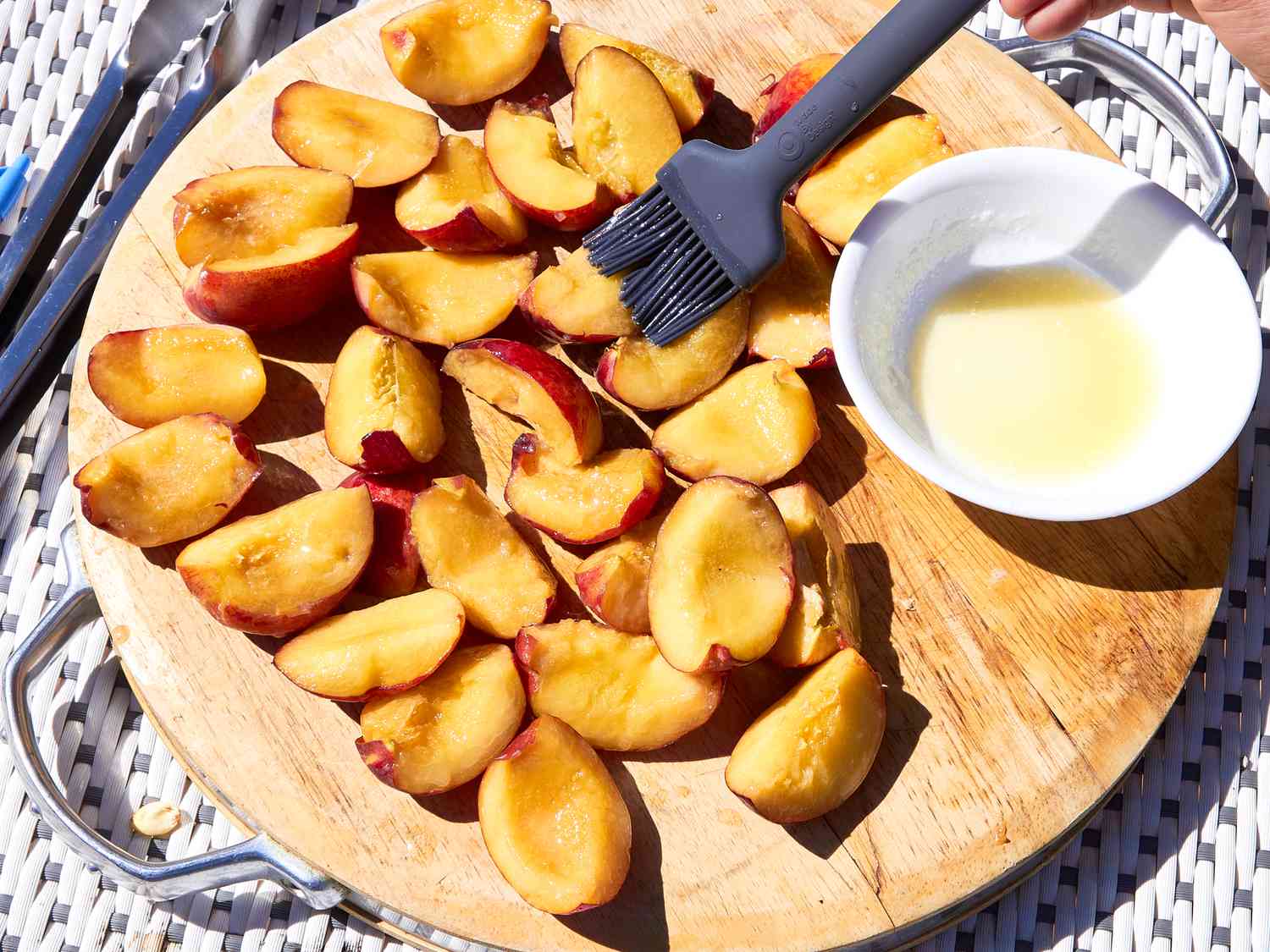 Sliced peaches on a wooden board with a bowl of dressing and a cooking brush