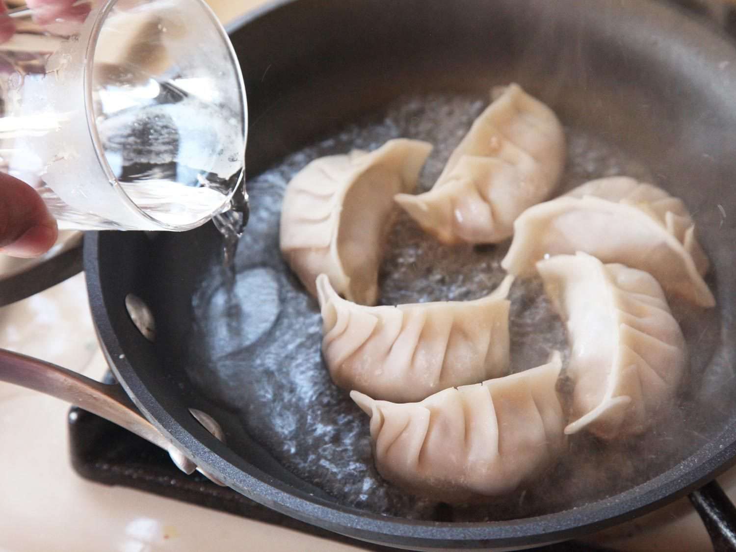 Adding water to a pan of frying dumplings.