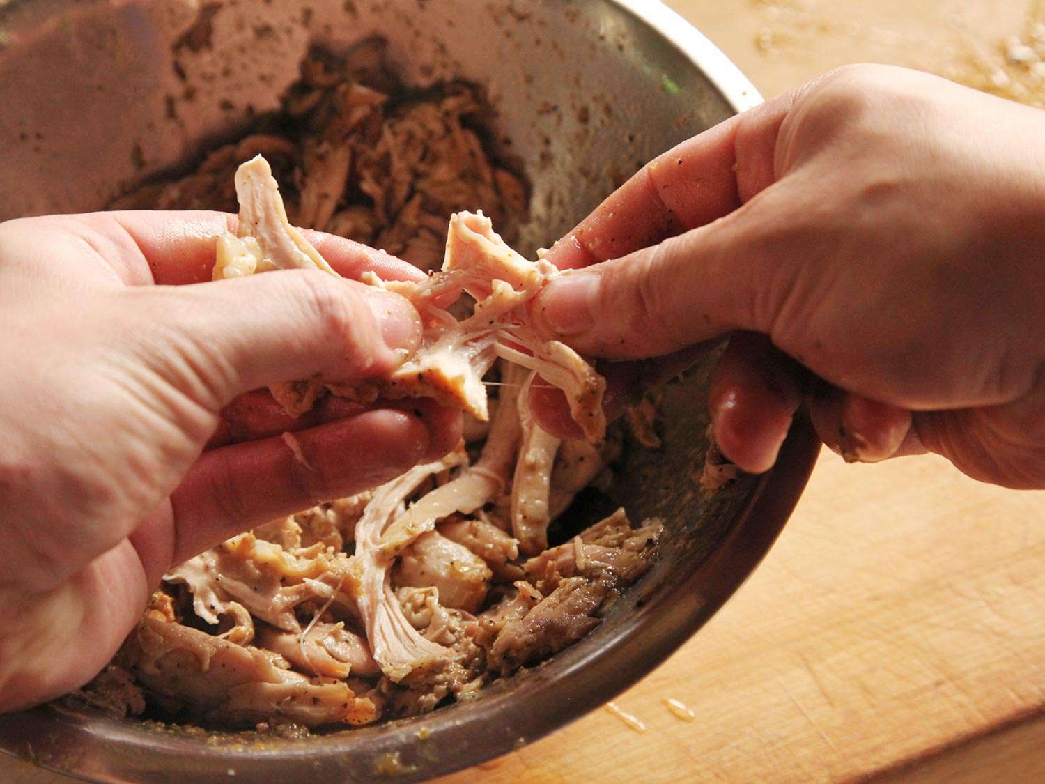 Cooked chicken is shredded in a bowl by hand.