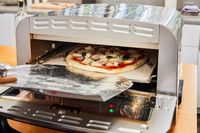A person places a pizza into the Cuisinart CPZ-120 Stainless Steel Indoor Pizza Oven