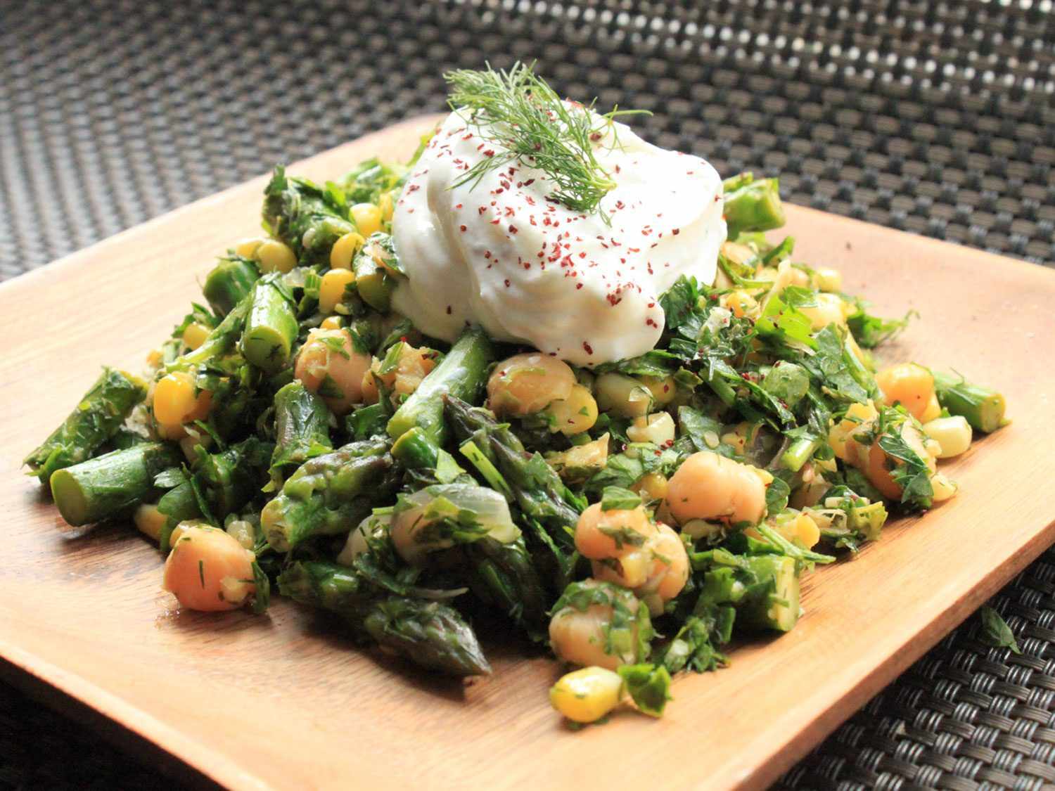 A plate of Fresh Herbs With Corn, Asparagus, and Chickpeas topped with a dollop of yogurt and fresh dill.