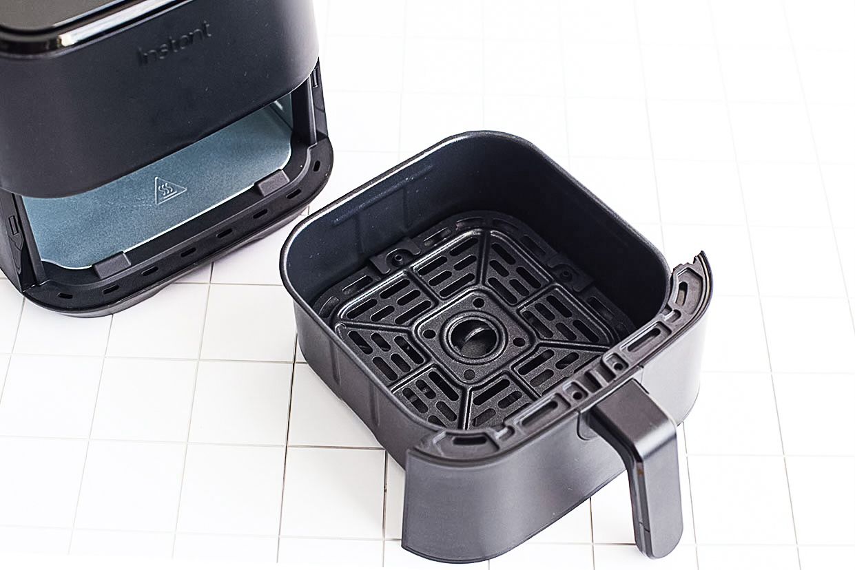 Parts of an air fryer disassembled on a countertop showing the basket and the base unit