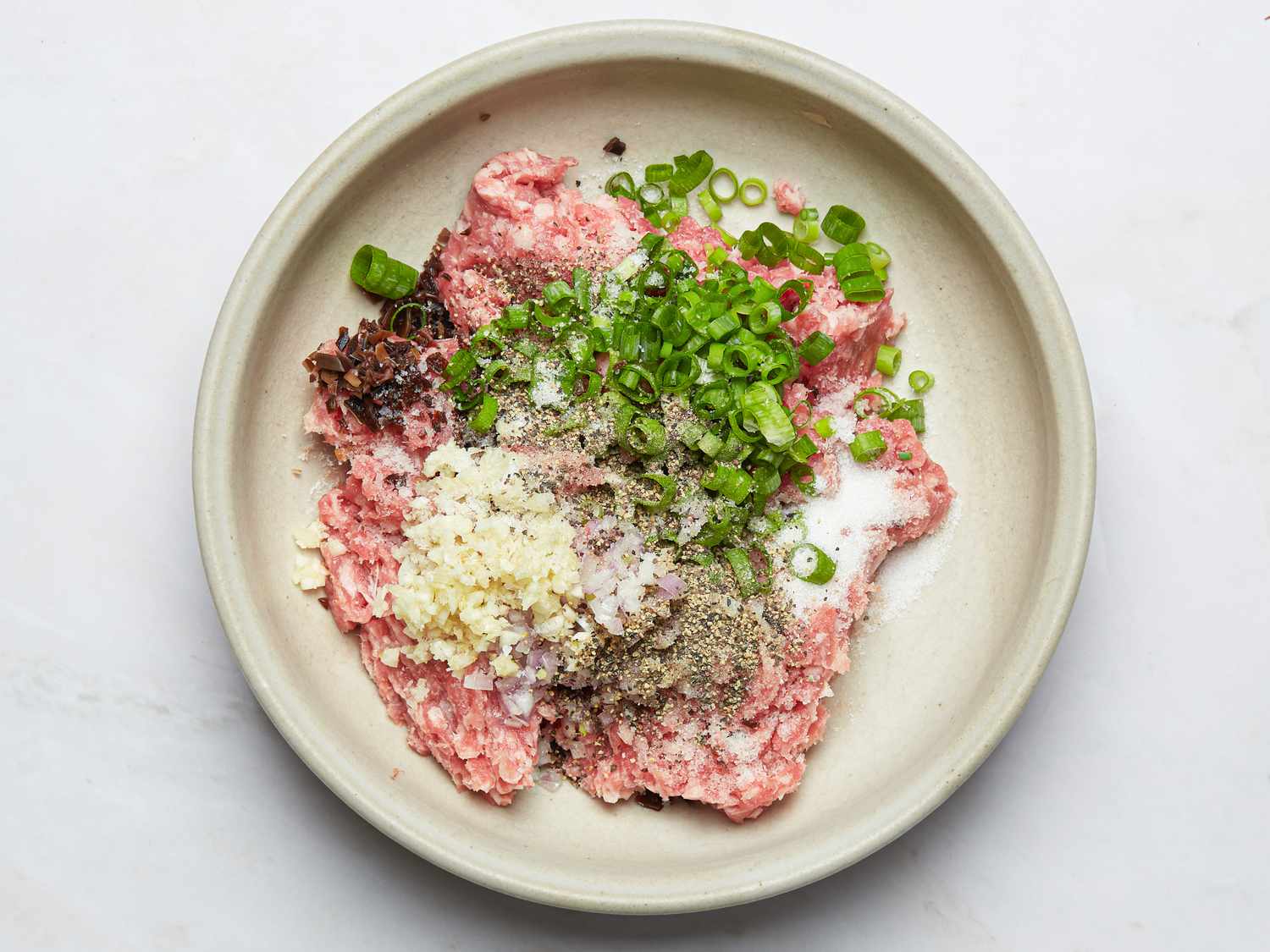 A bowl with ground pork mixed with chopped green onions, minced garlic, and black pepper before cooking