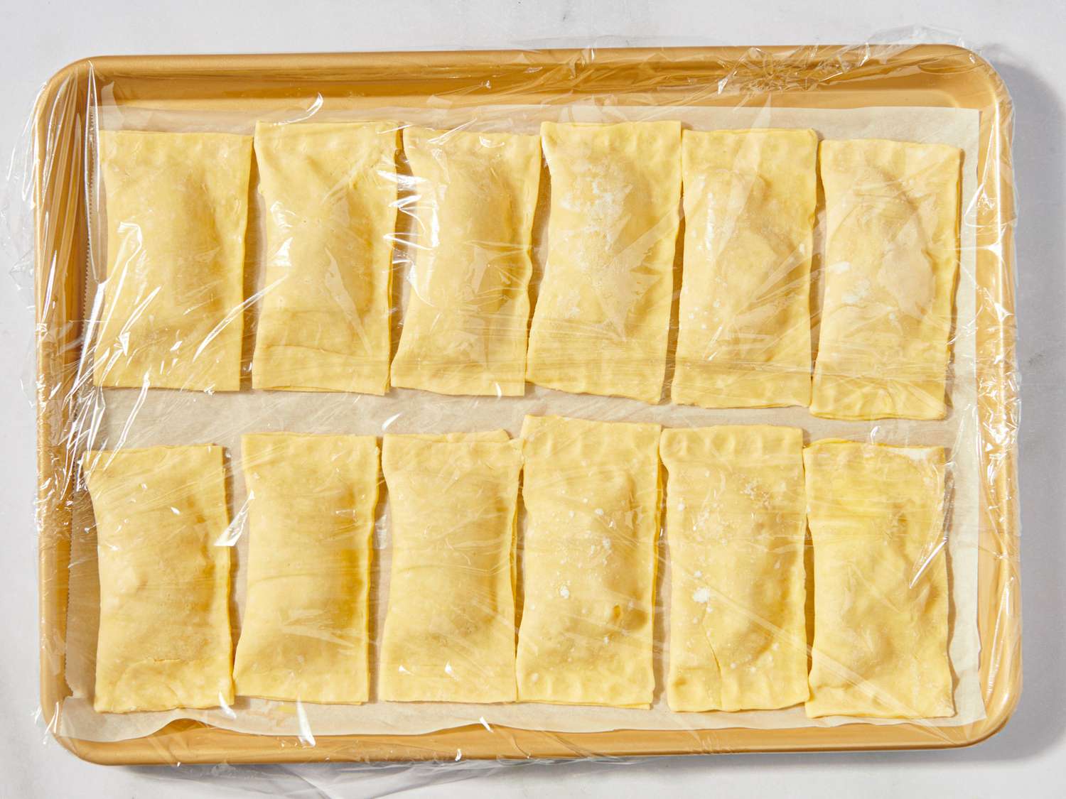 Tray of uncooked apple hand pies covered with plastic wrap