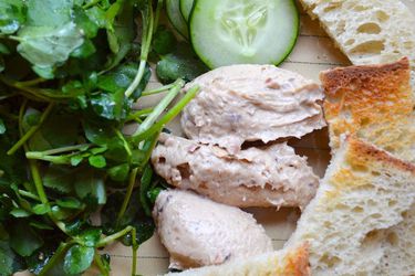 Closeup of several quenelles of gentleman's relish surrounded by toasts, cucumber slices, and watercress.