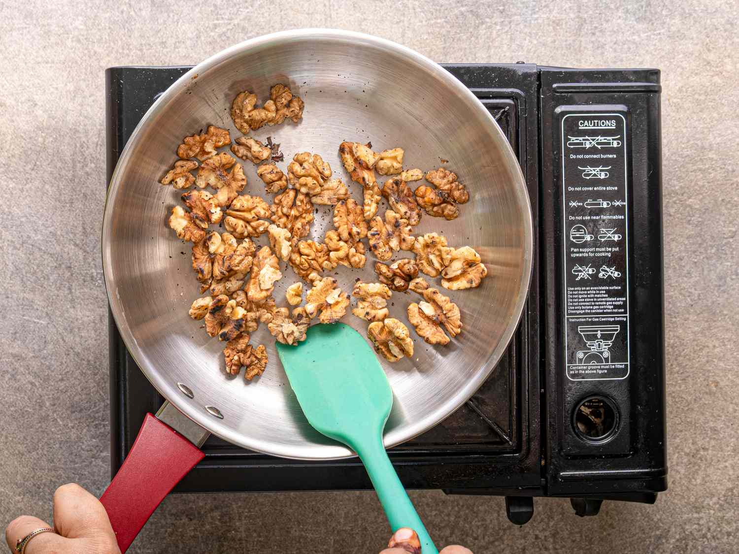 Toasting walnuts in a skillet with a green spatula over a singleburner stove