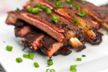 Closeup of Cajun-Spiced Barbecue Ribs, served on a white platter and showered with chopped scallion.