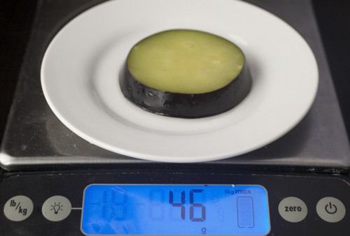 A slice of eggplant is weighed on a digital scale. The scale reads 46 grams.