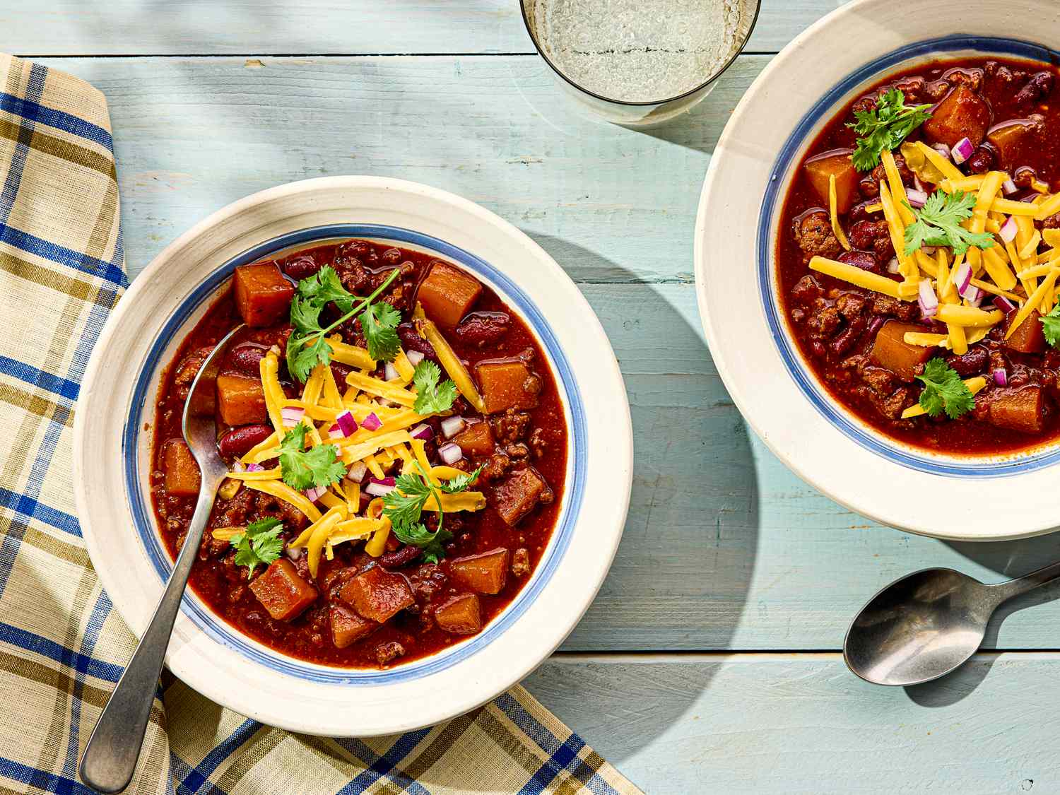 Two bowls of turkey chili with toppings spoons and a napkin on a table