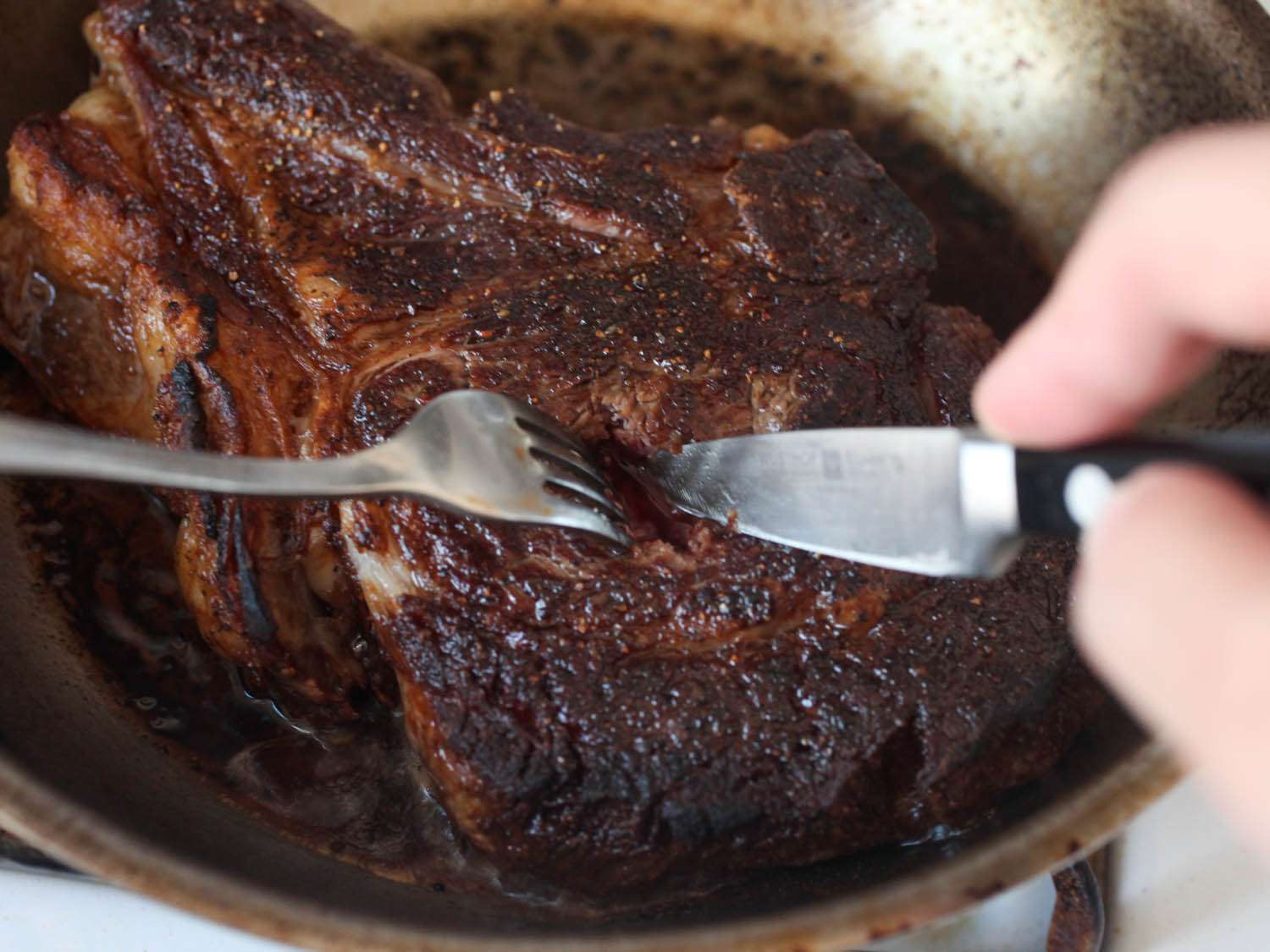 Slicing a steak in the pan to check doneness.