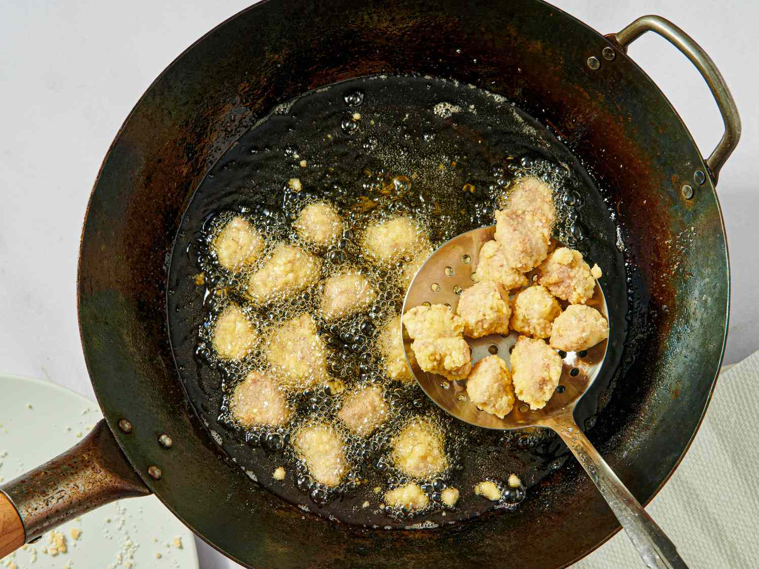 Chunks of battered pork being fried in a large wok with oil a slotted spoon lifting portions out