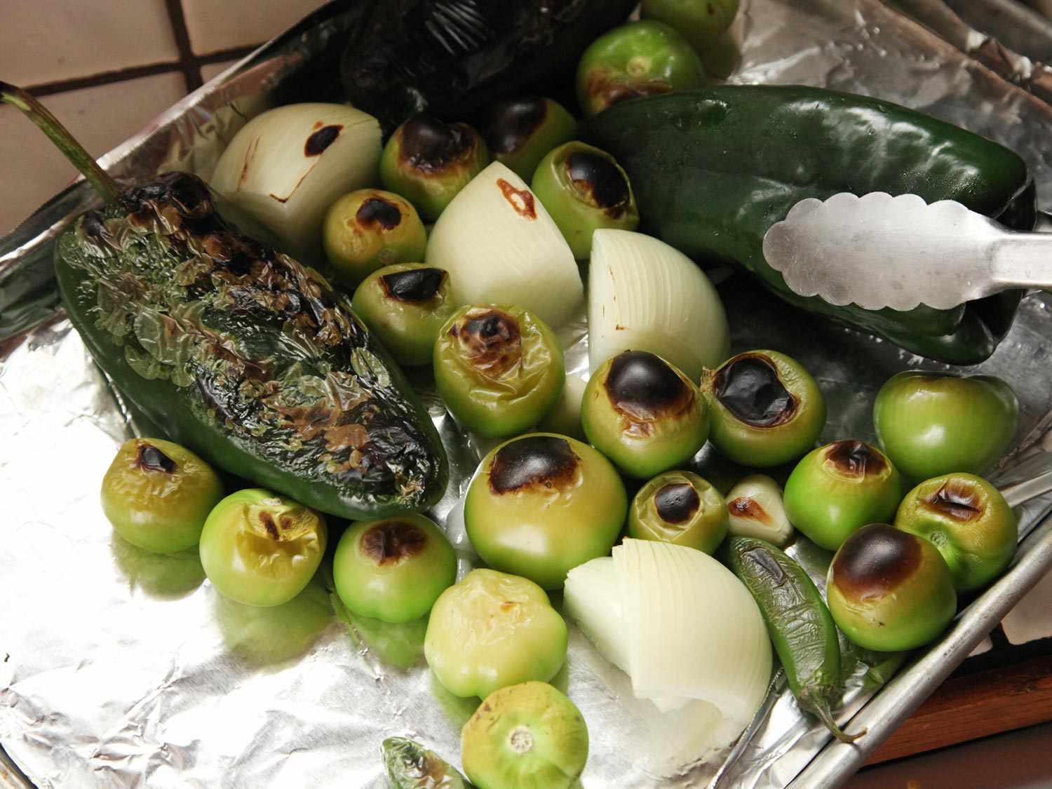Salsa ingredients have been broiled on one side and are being turned with a pair of tongs.