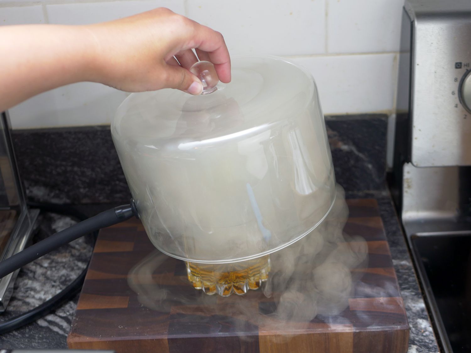 a hand lifting the cloche off an Old Fashioned