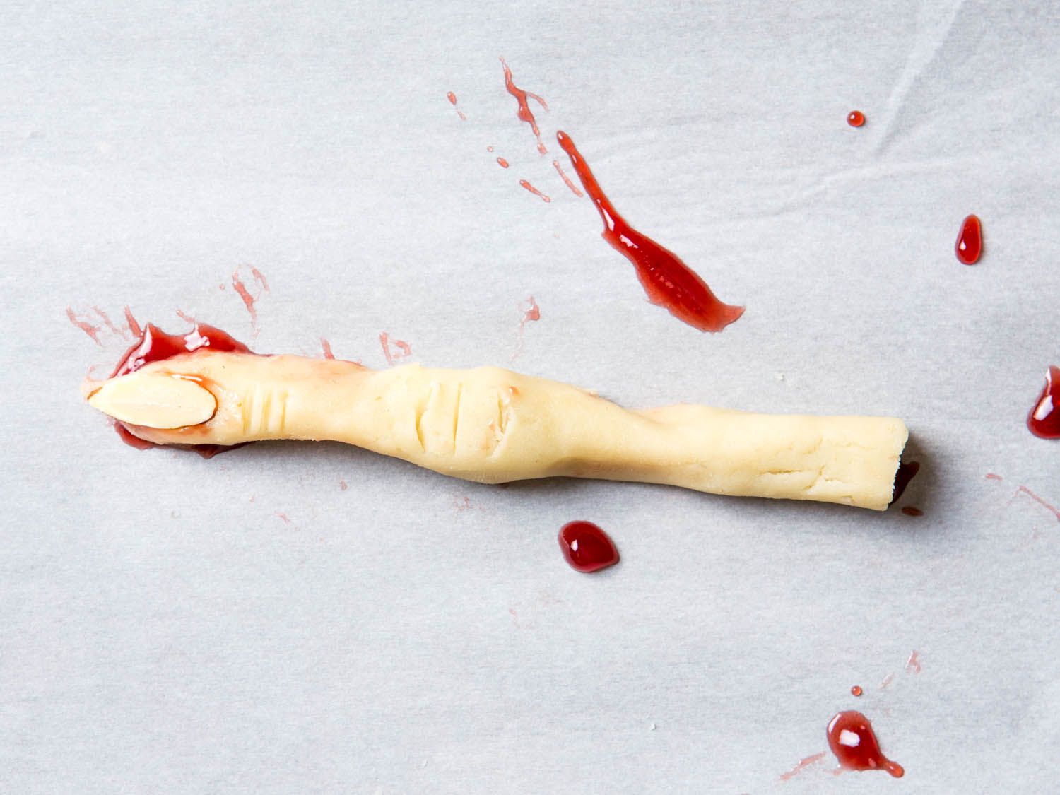 A witch finger shortbread cookie with drops of raspberry jam to resemble blood.