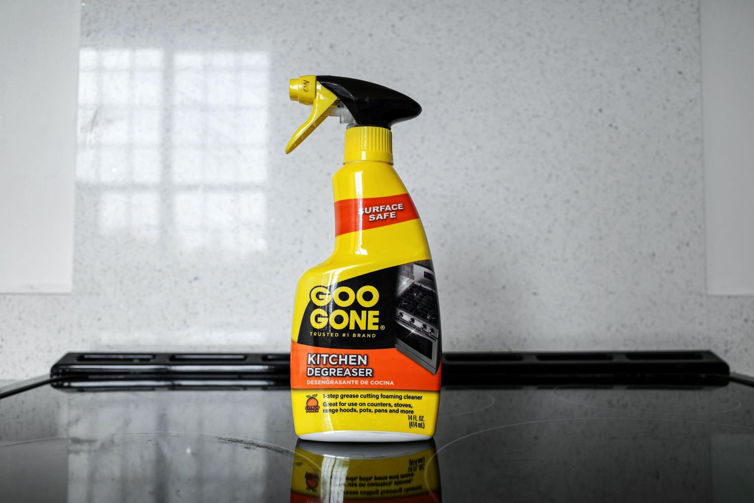 A bottle of Goo Gone Kitchen Degreaser placed on a stovetop in front of a tiled backsplash