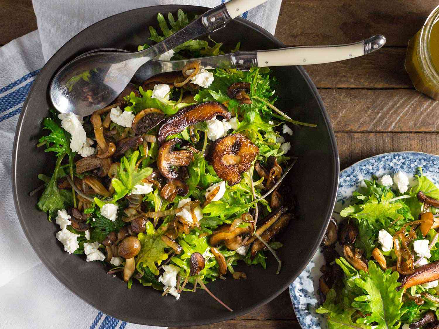 Caramelized mushrooms and kale salad on a black plate, sprinked with goat's cheese pieces.