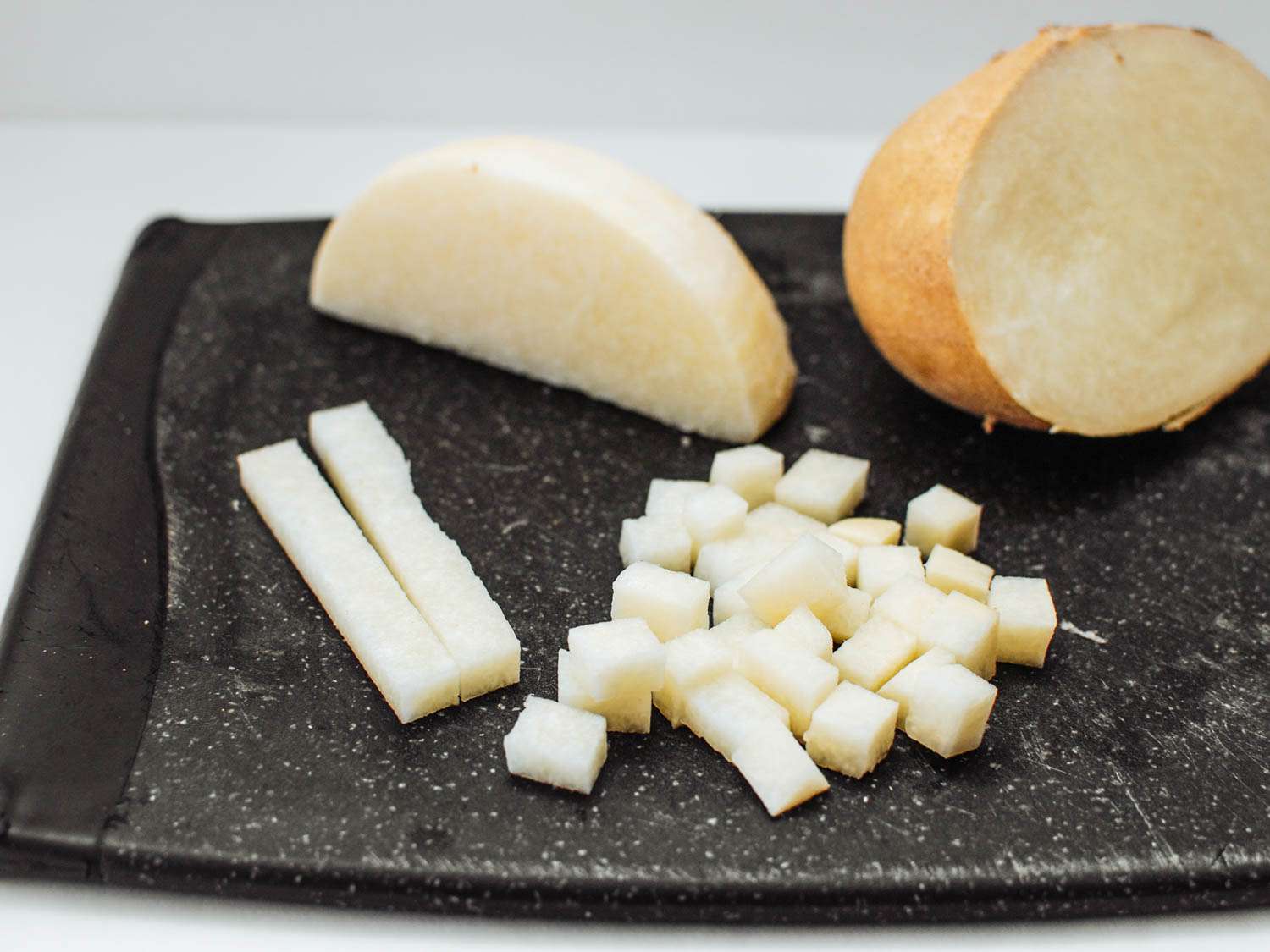 A platter showing a halved jicama with peel, a half slice, sticks, and cubes.