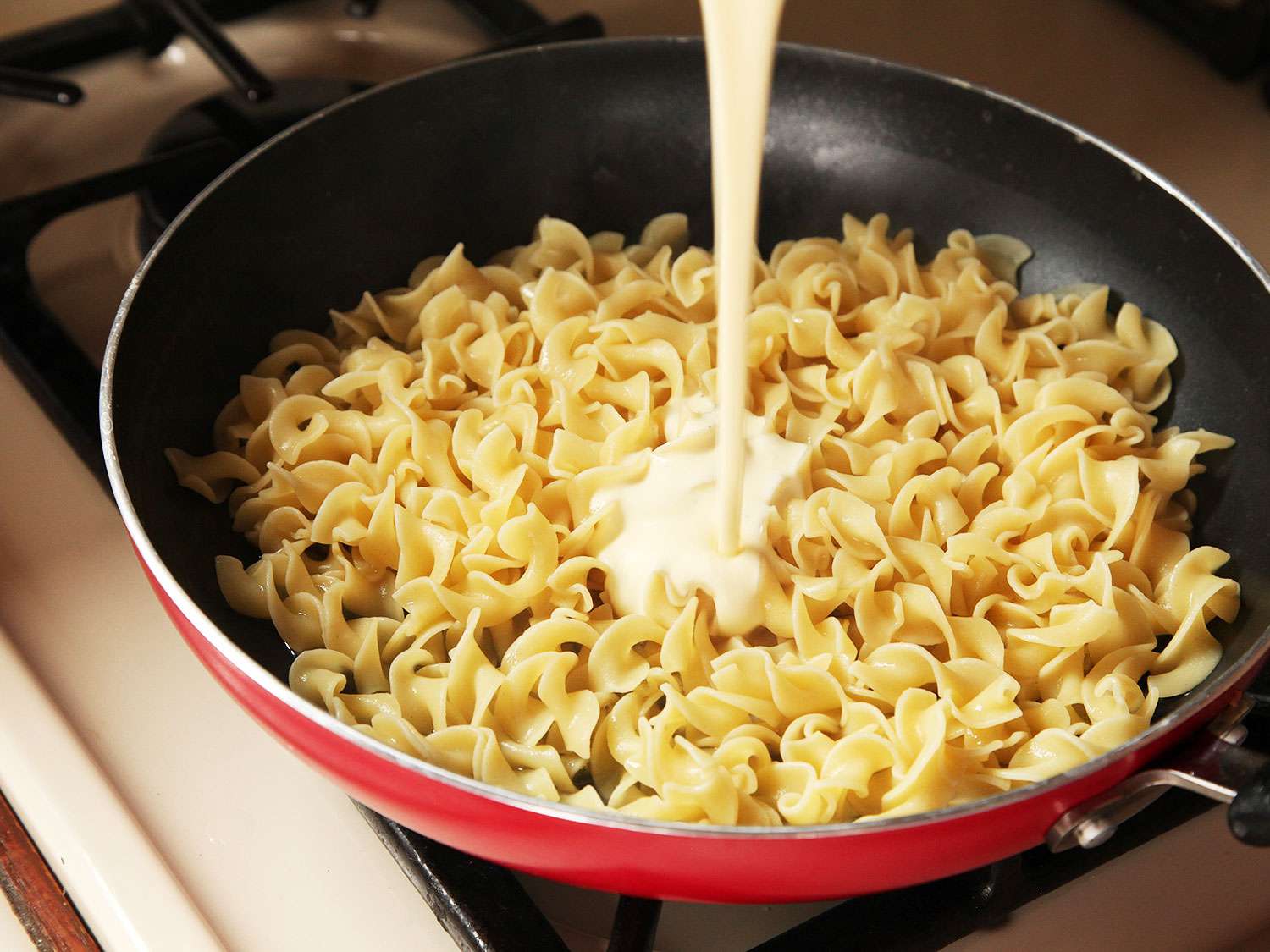 Pouring the sauce into the skillet containing pasta. 