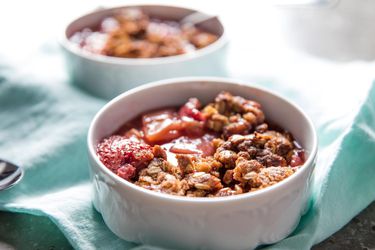 Two bowls of strawberry-rhubarb crisp, served on a light blue cloth.