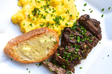 Overhead view of a plate of Herb-Marinated Steak and Soft Scrambled Eggs, served with a slice of buttered toast and showered with chopped chives.