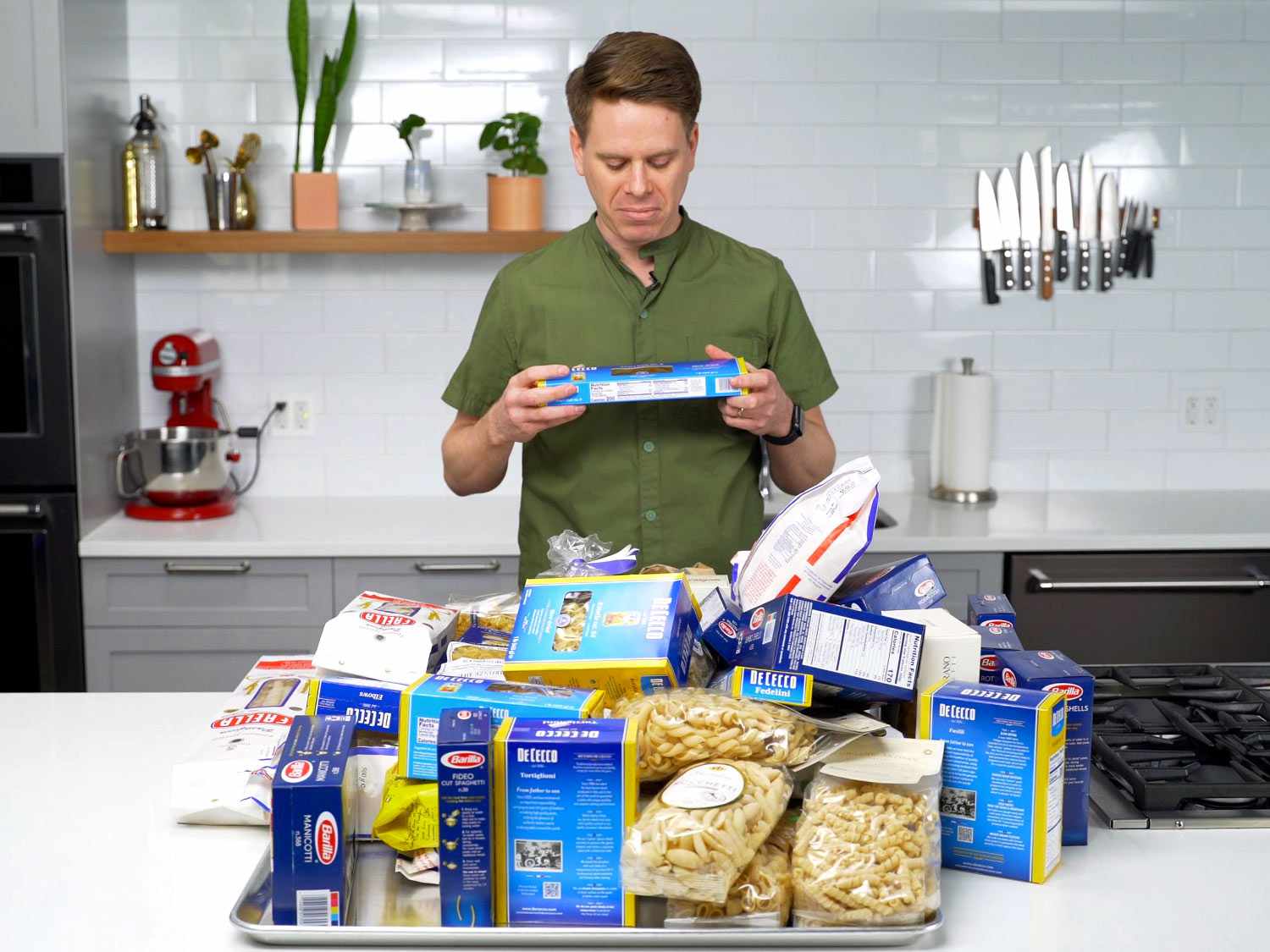 Sasha Marx standing in front of a pile of pasta products while frowning at a box of angel hair