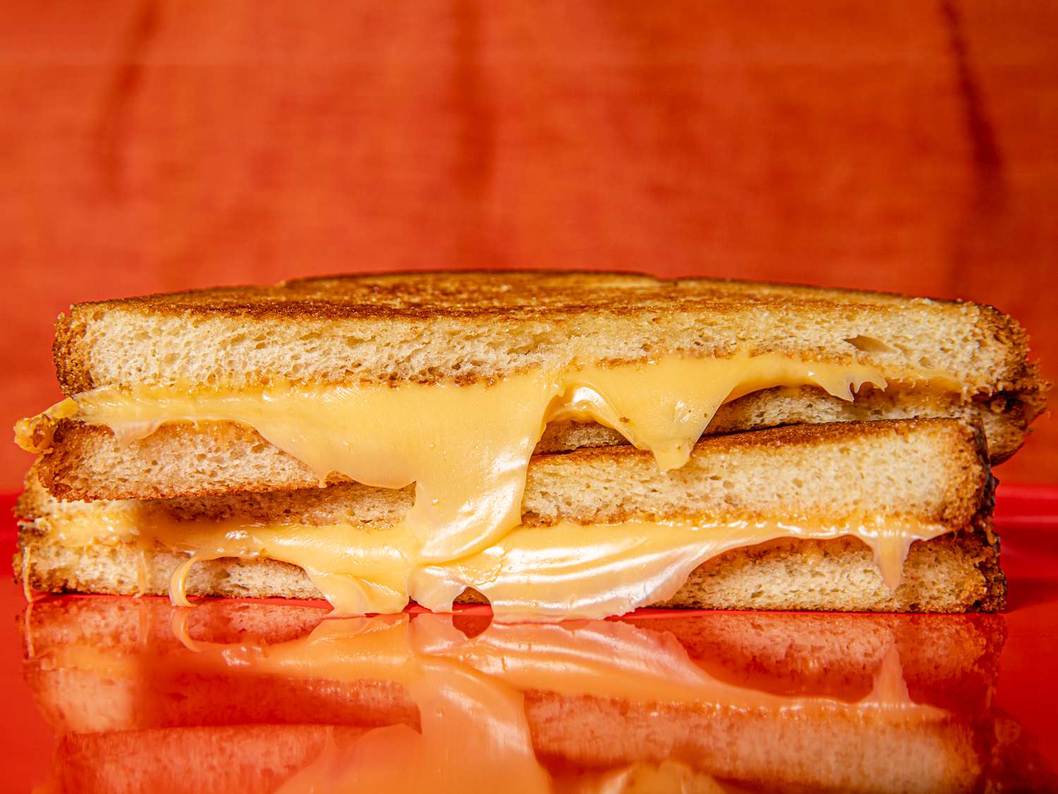 Two halfs of a grilled cheese stacked on top of each other with cheese dripping down the front